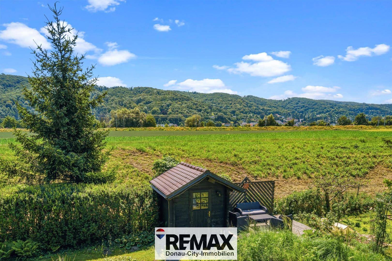 Kleines Gartenhaus mit Sitzbereich und weitem Blick über Felder und Hügel.