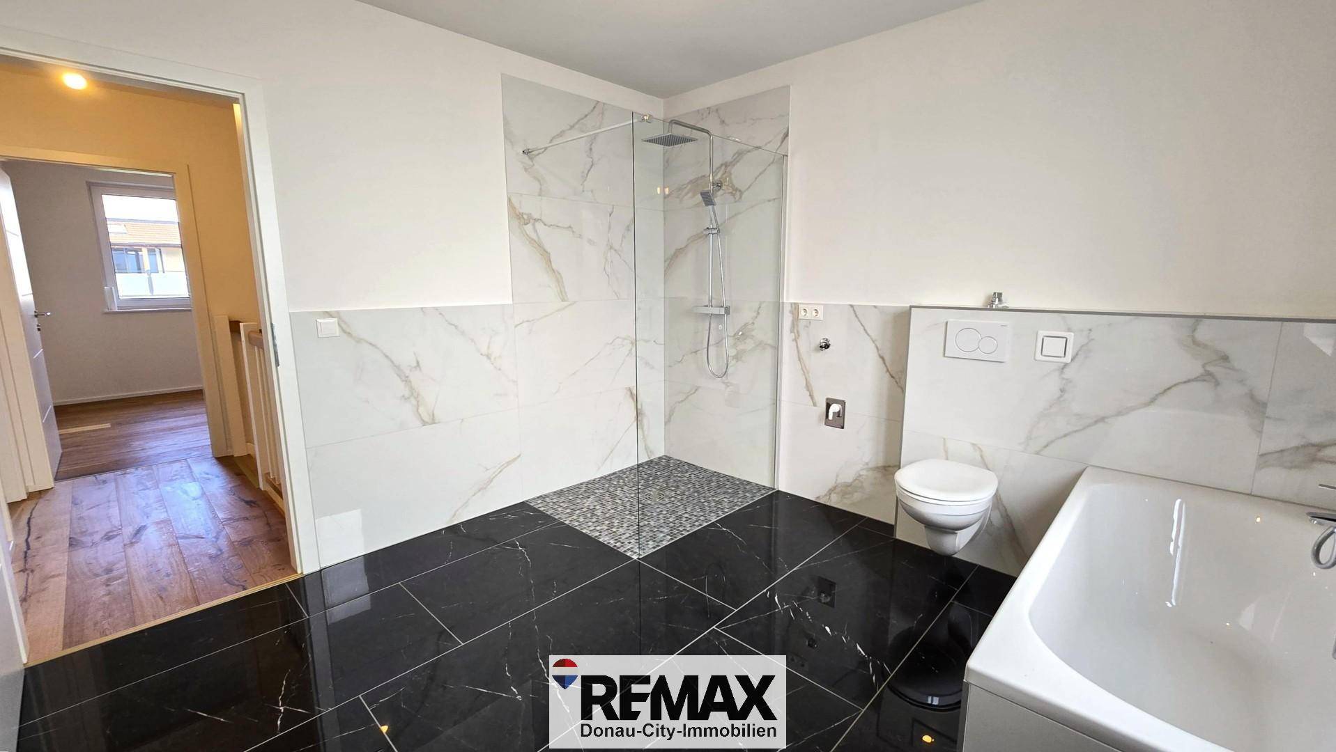 Modernes Badezimmer mit begehbarer Dusche, Badewanne und eleganten Marmorfliesen an den Wänden.