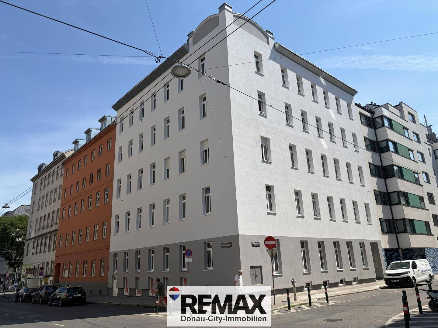 Mehrstöckiges Eckgebäude mit weißer und oranger Fassade an einer belebten Stadtstraße.