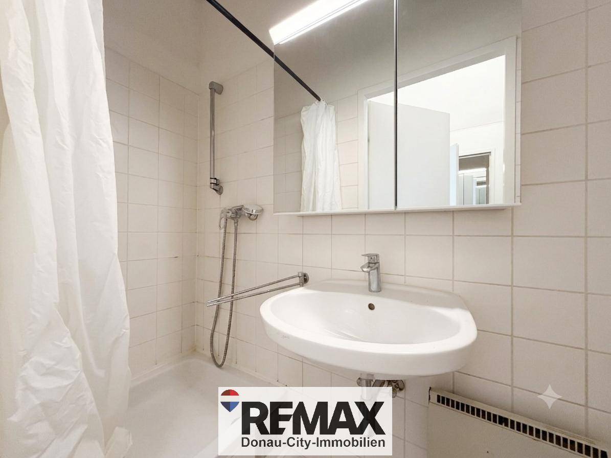 Badezimmer mit Waschbecken, Spiegelschrank und Duschbereich mit Vorhang, komplett gefliest.