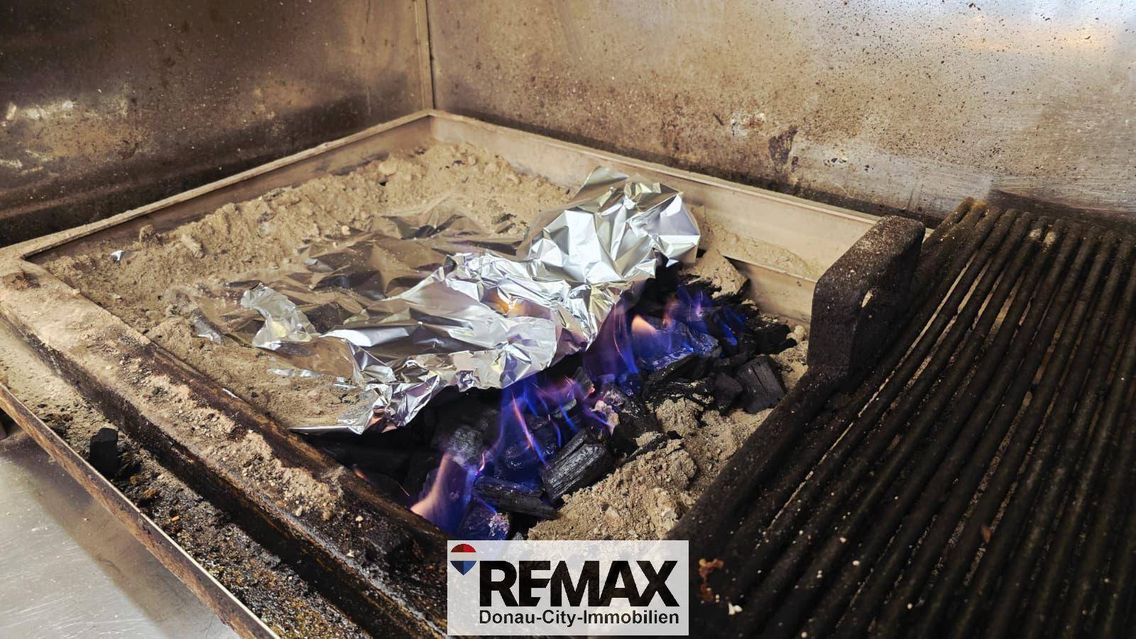 Nahaufnahme eines Grills mit brennender Holzkohle und Alufolie, bereit für die Zubereitung von Speisen.