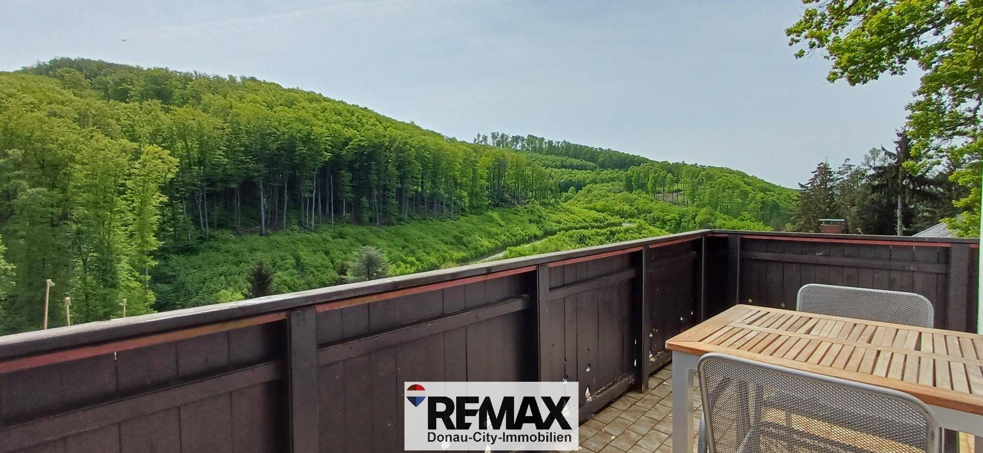 Balkon mit Holzboden und Sitzgelegenheiten, bietet einen weiten Blick auf bewaldete Hügel.