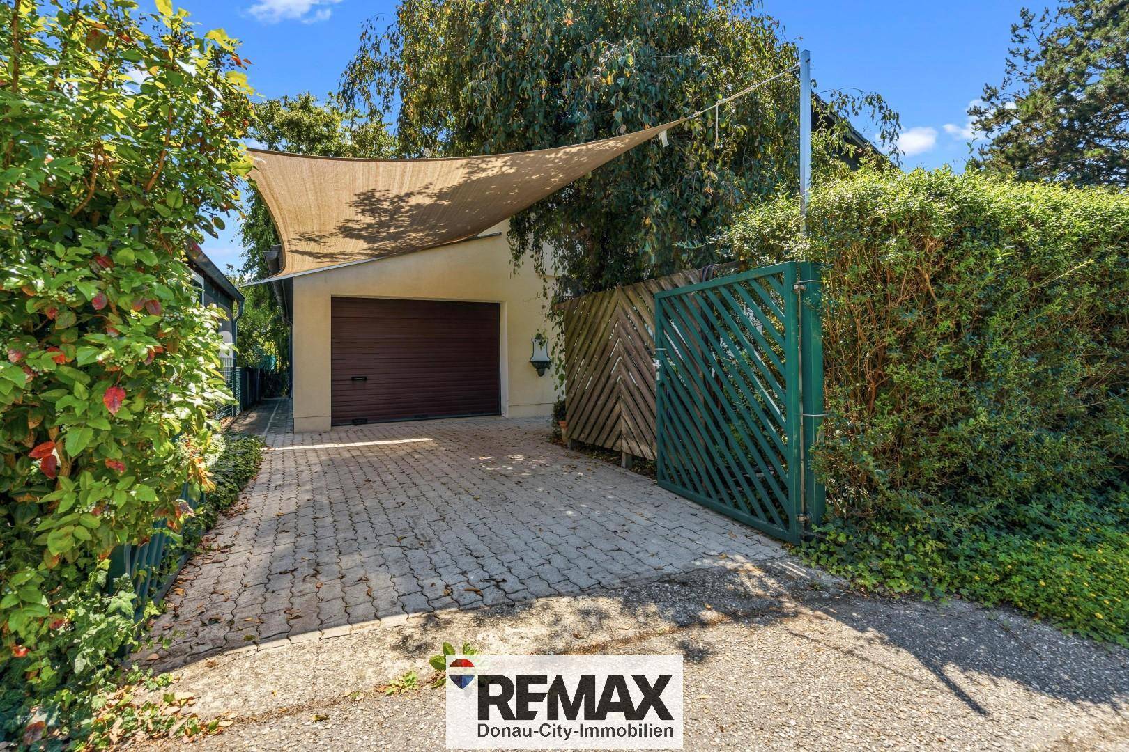 Einfahrt mit gepflastertem Weg, Garage und Carport unter einem Sonnensegel.