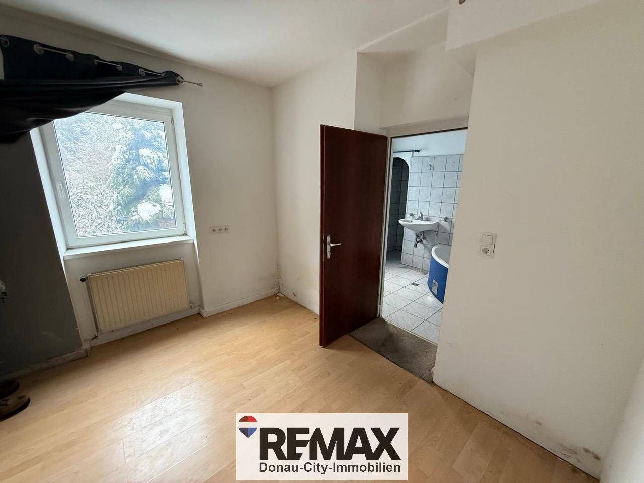 Schlafzimmer mit Laminatboden und Zugang zu einem angrenzenden Badezimmer, das renovierungsbedürftig ist.