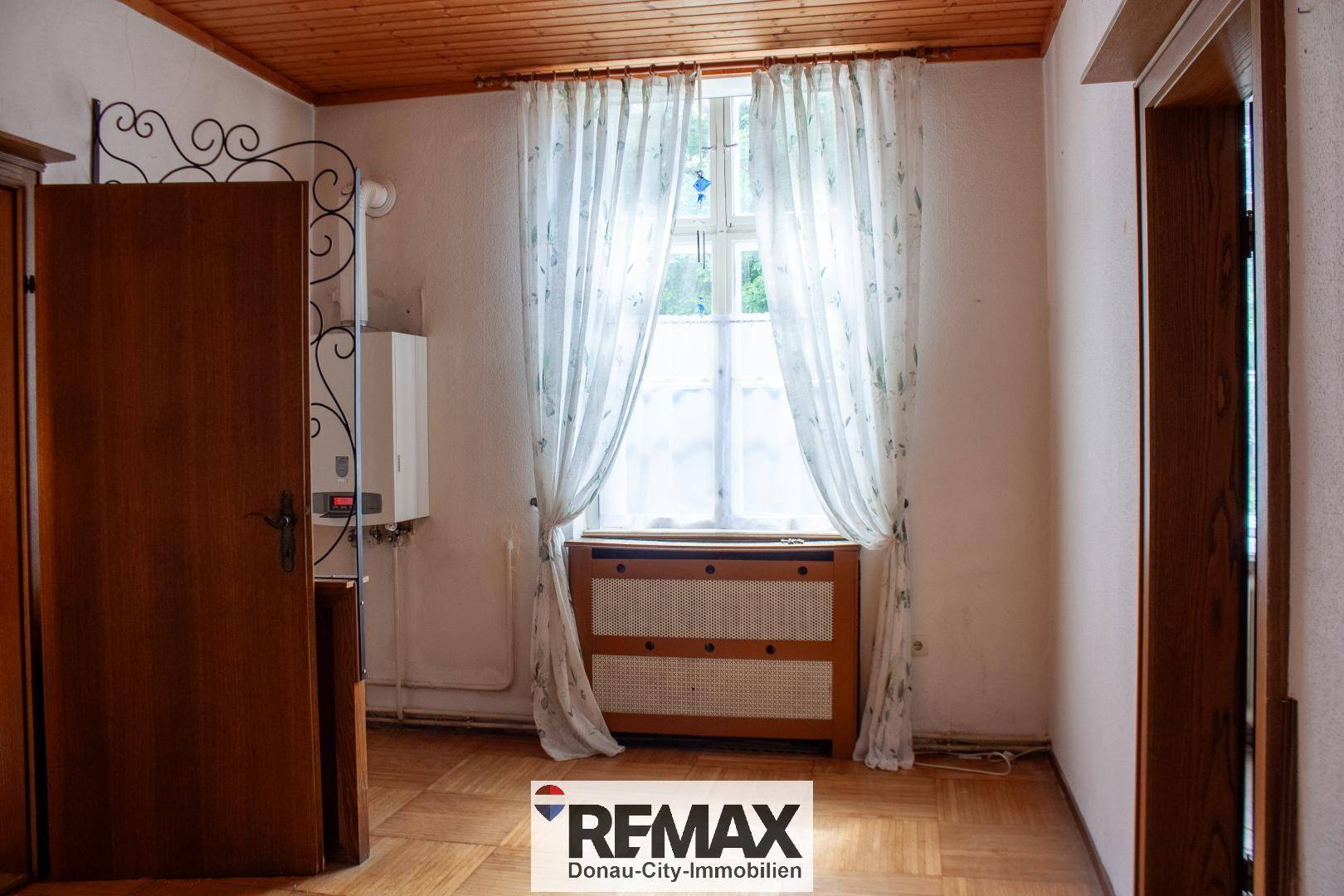 Heller Flur mit Holzparkettboden, einem Fenster und einem Heizkessel an der Wand.