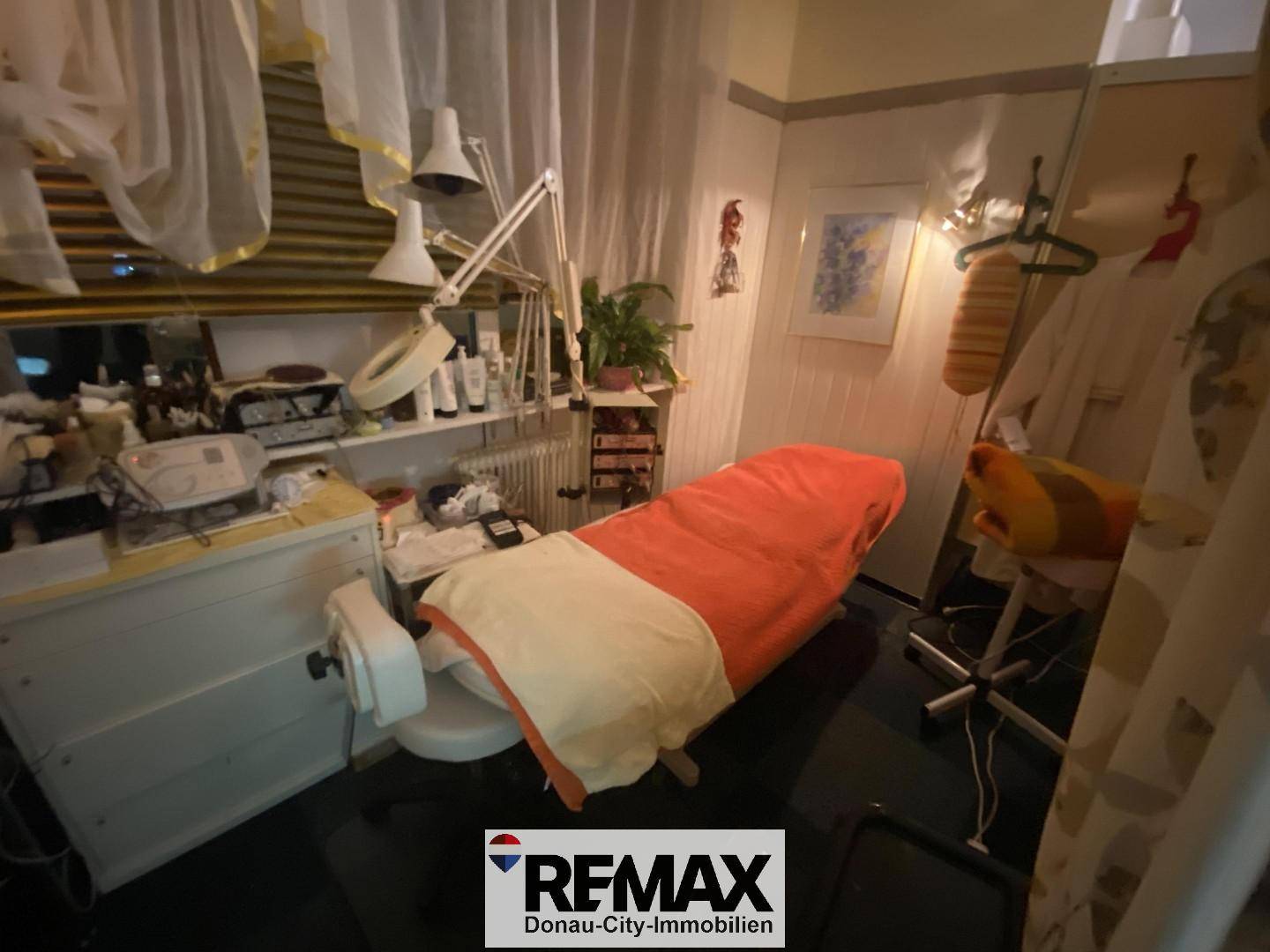 Behandlungsraum mit orangefarbener Liege, Beleuchtung und Spiegel an der Wand.
