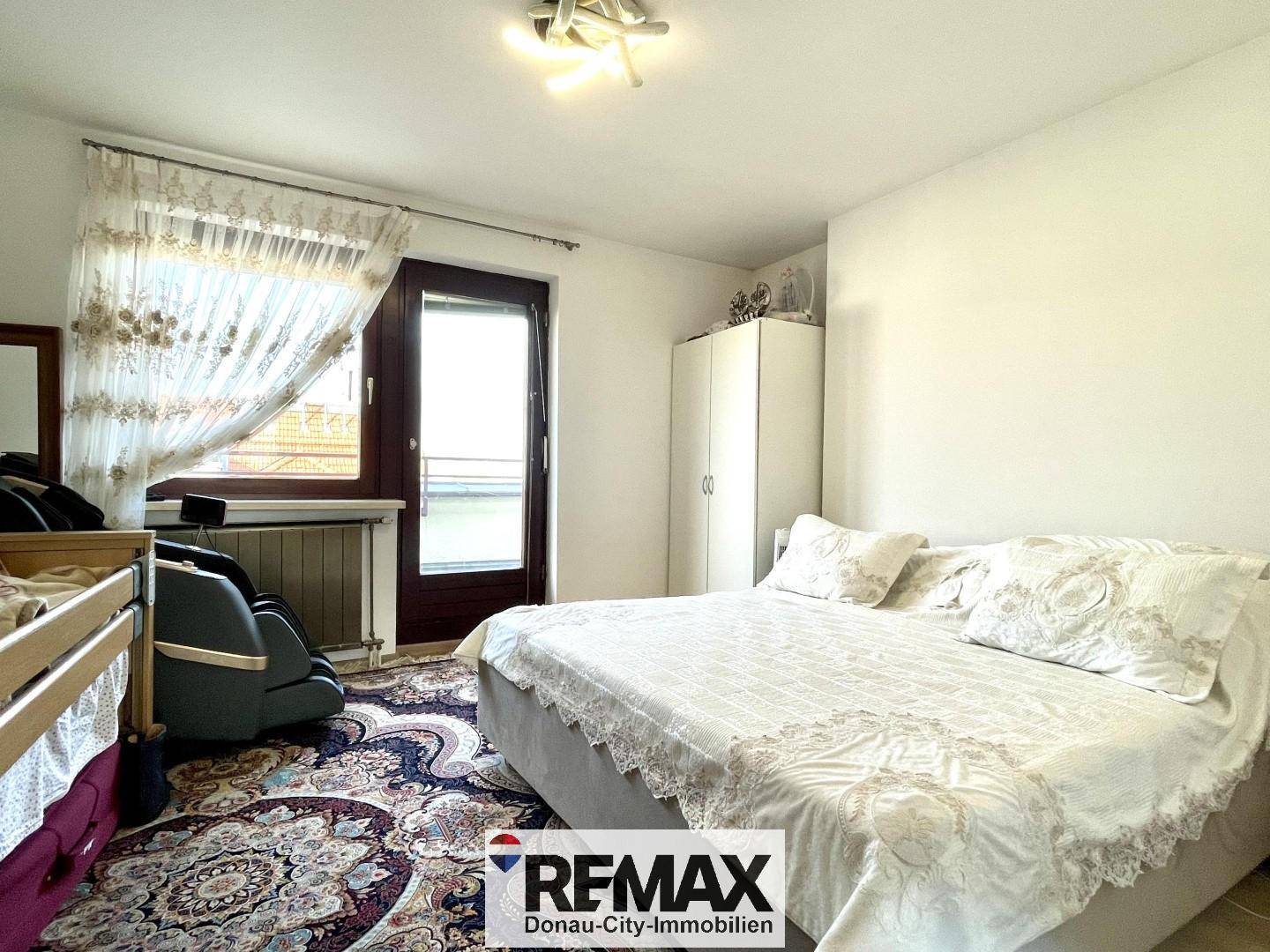 Helles Schlafzimmer mit großem Bett, weißem Kleiderschrank und Zugang zu einem Außenbereich.