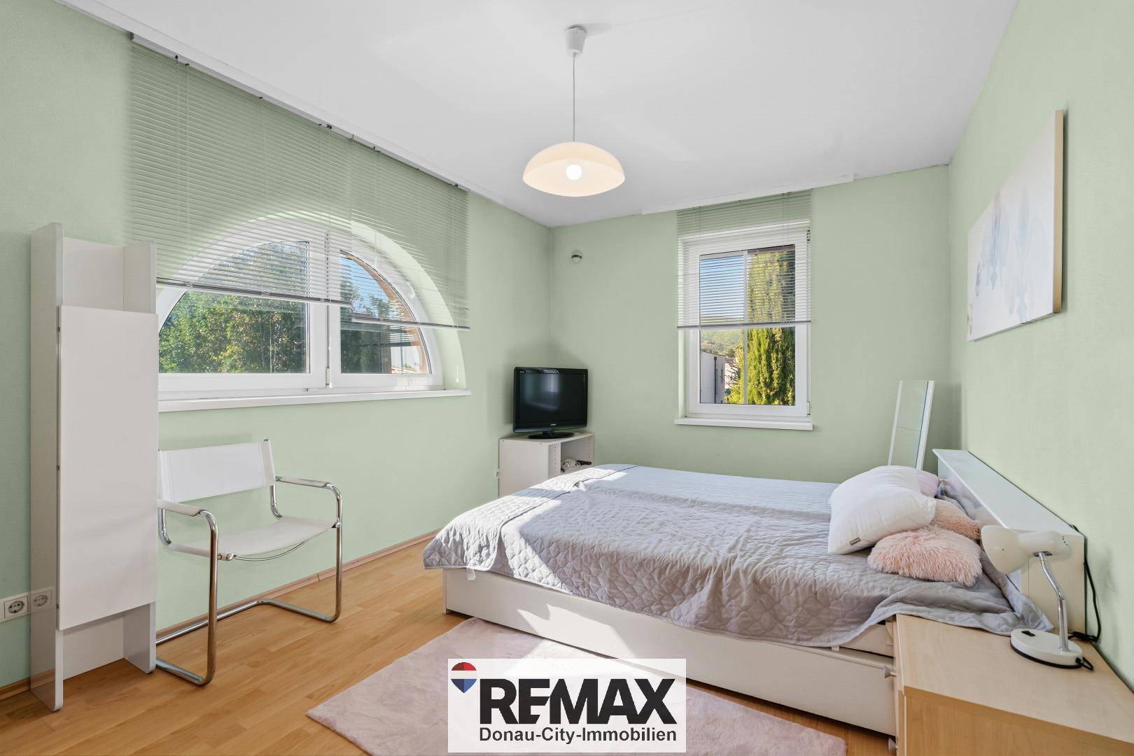 Helles Schlafzimmer mit Holzfußboden, großen Fenstern und Blick ins Grüne.