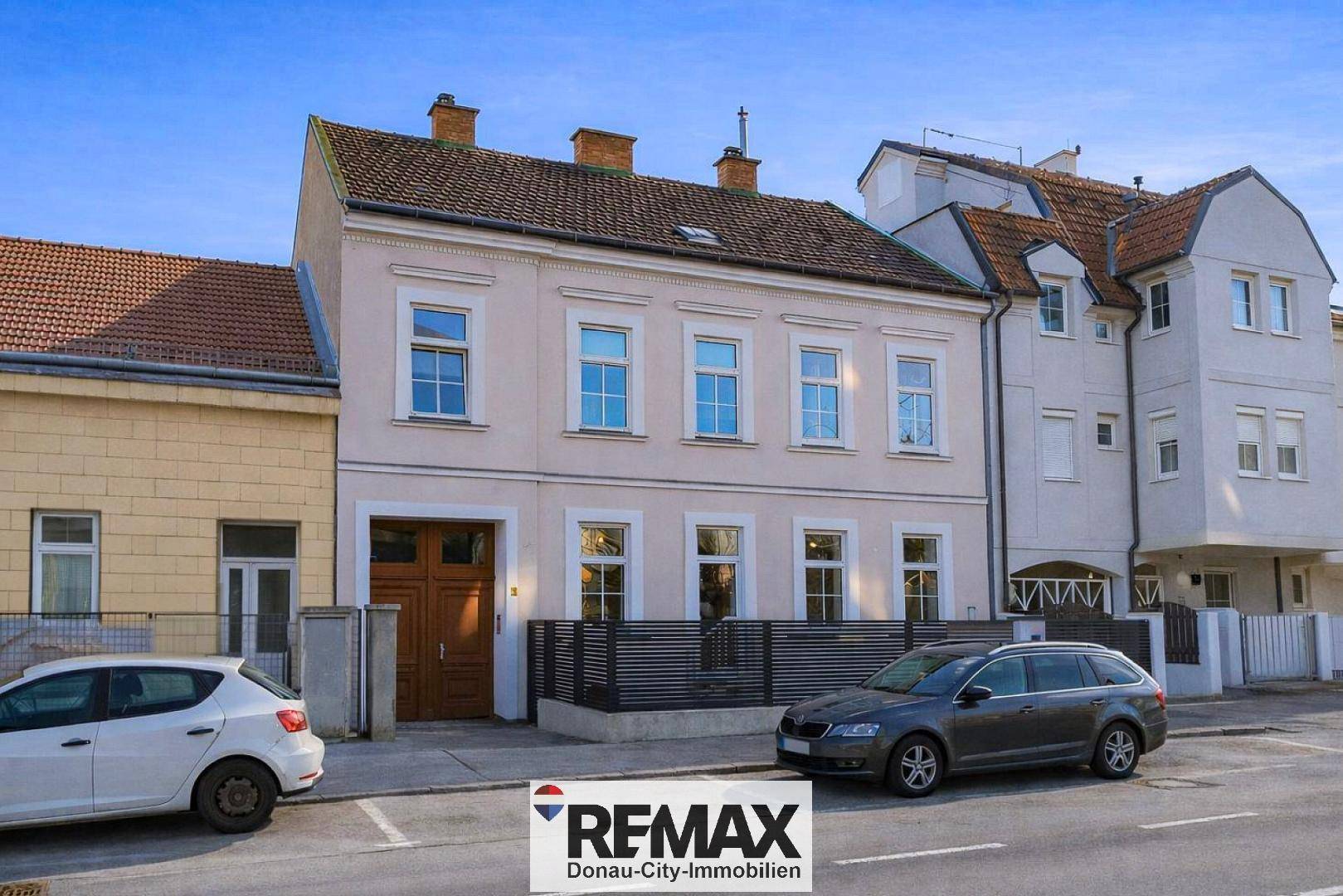 Klassische Hausfassade mit mehreren Fenstern und geparkten Autos auf der Straße.