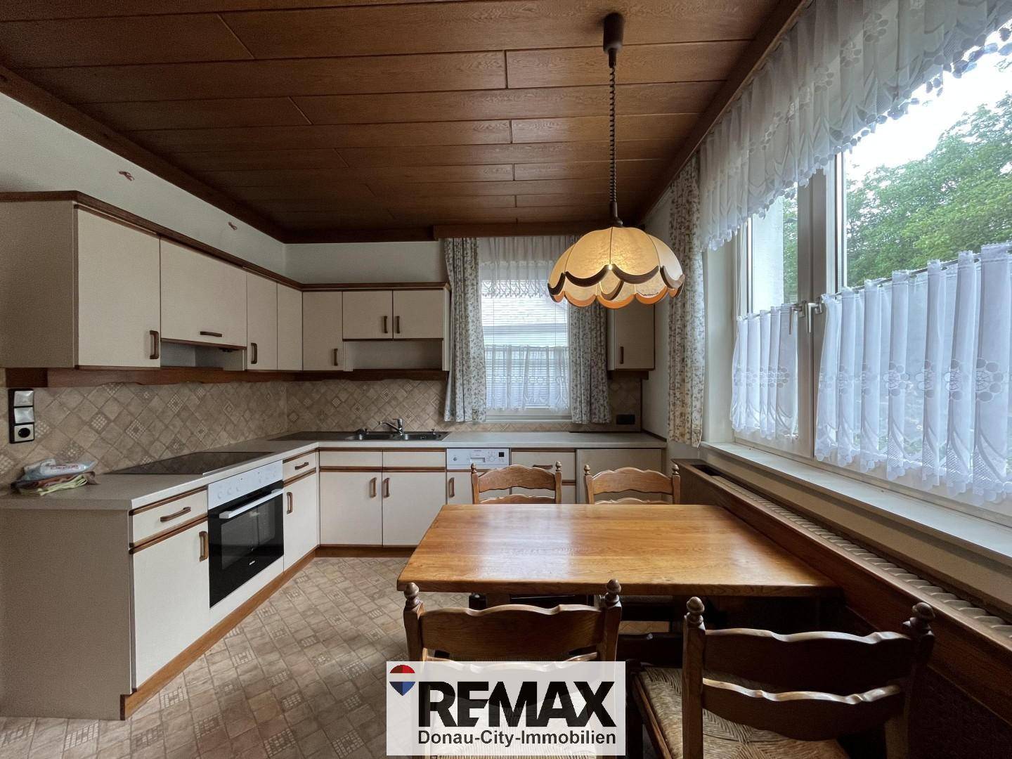 Traditionelle Küche mit Holzdecke, Einbauschränken und Essbereich am Fenster.