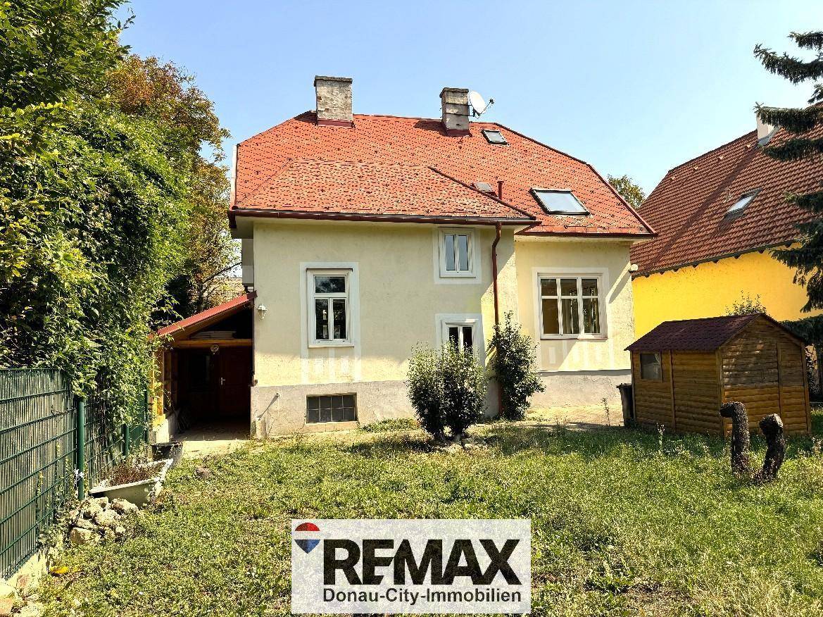 Seitenansicht des Hauses mit Garten, einem kleinen Schuppen und einem überdachten Bereich.