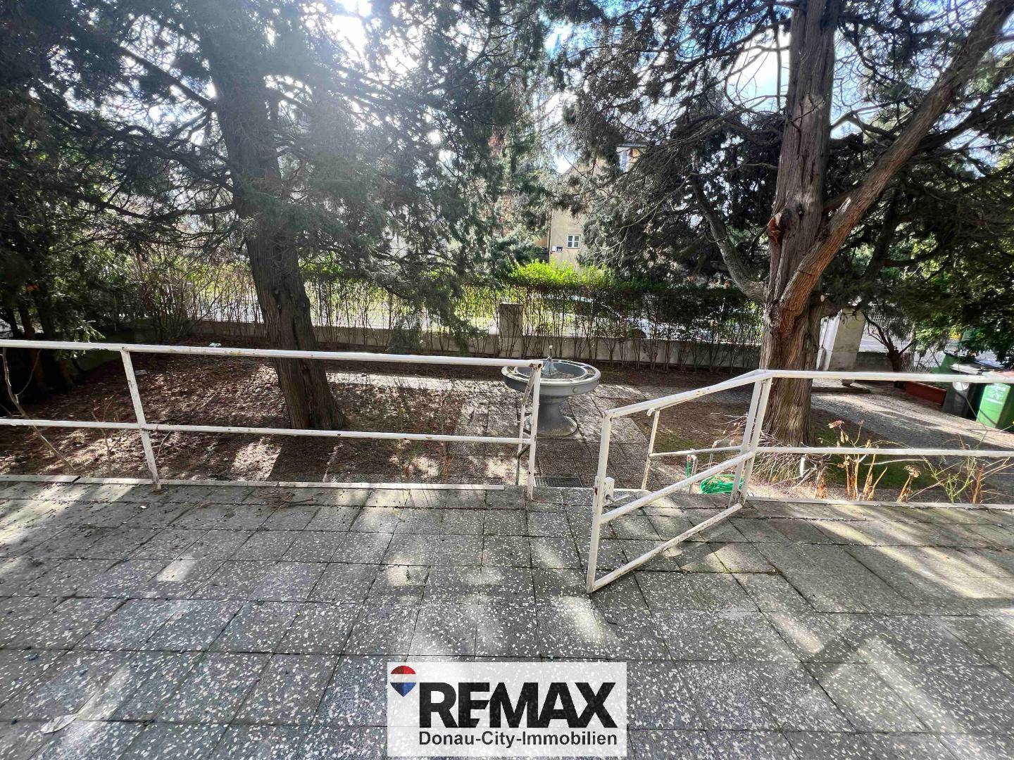 Gepflasterte Terrasse mit Geländer und Blick auf den Gartenbereich mit Bäumen.