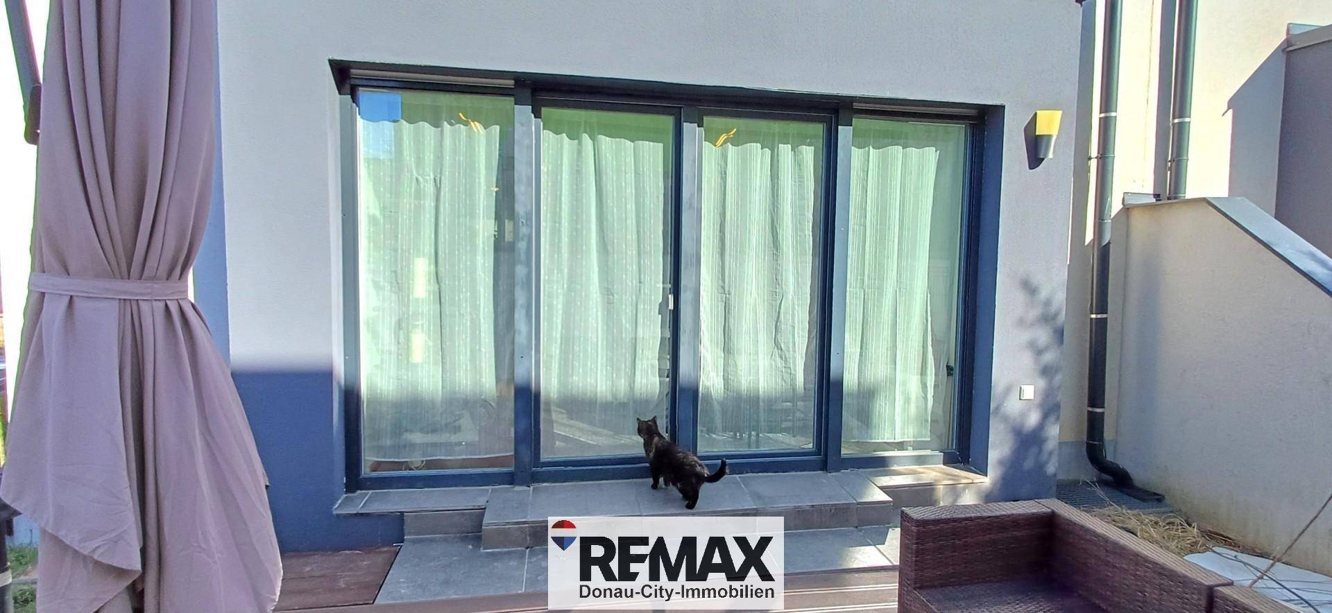 Gebäudefassade mit großen Schiebetüren, die zu einer Terrasse führen.