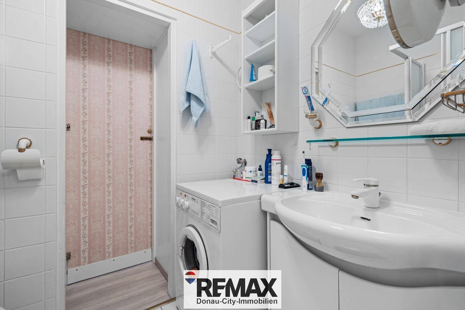 Kleines Badezimmer mit Waschbecken, Waschmaschine und weißen Fliesen.
