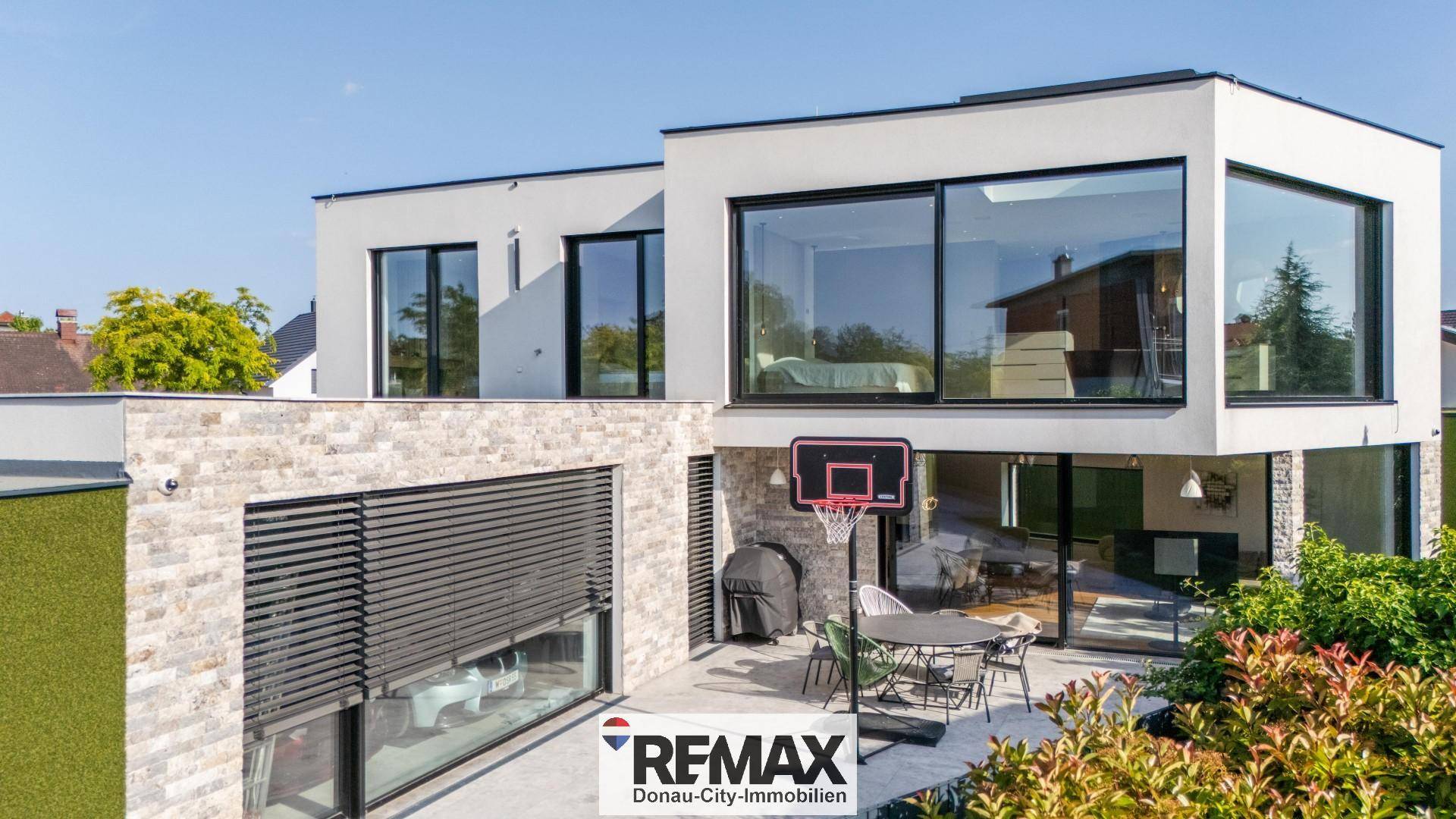 Terrasse mit Basketballkorb, Gartenmöbeln und Blick auf die moderne Architektur des Hauses.