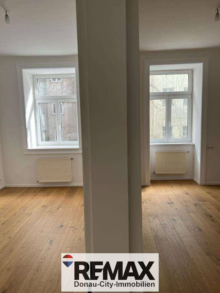 Lichtdurchflutetes Wohnzimmer mit Holzboden und zwei großen Fenstern.