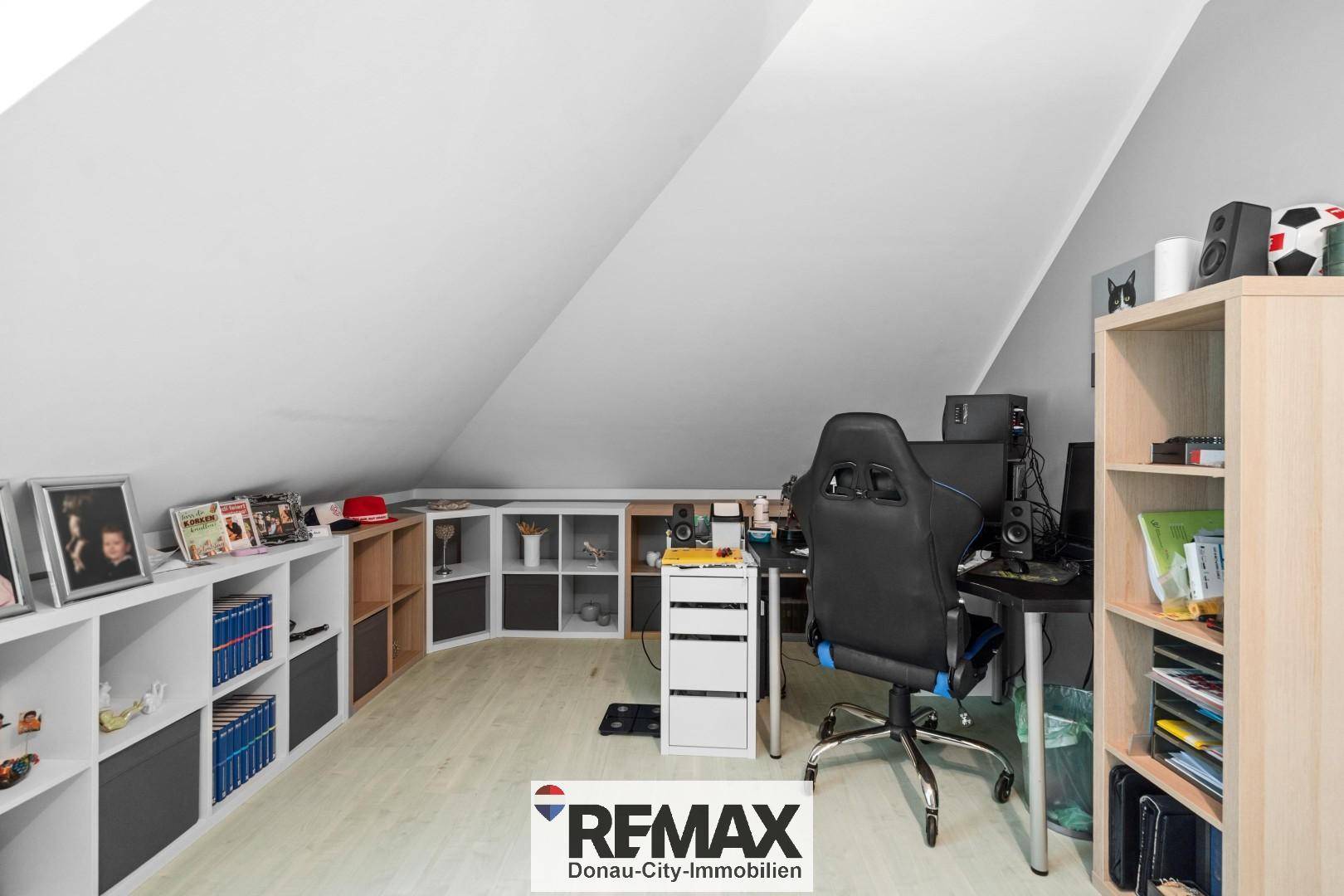 Helles Arbeitszimmer im Dachgeschoss mit Dachschrägen, Regalsystemen und Schreibtisch für kreative Tätigkeiten.