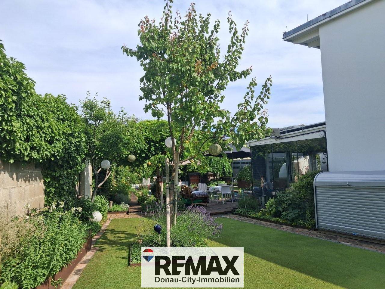 Gepflegter Garten mit Rasenfläche, Bäumen und einem Weg entlang des Hauses.