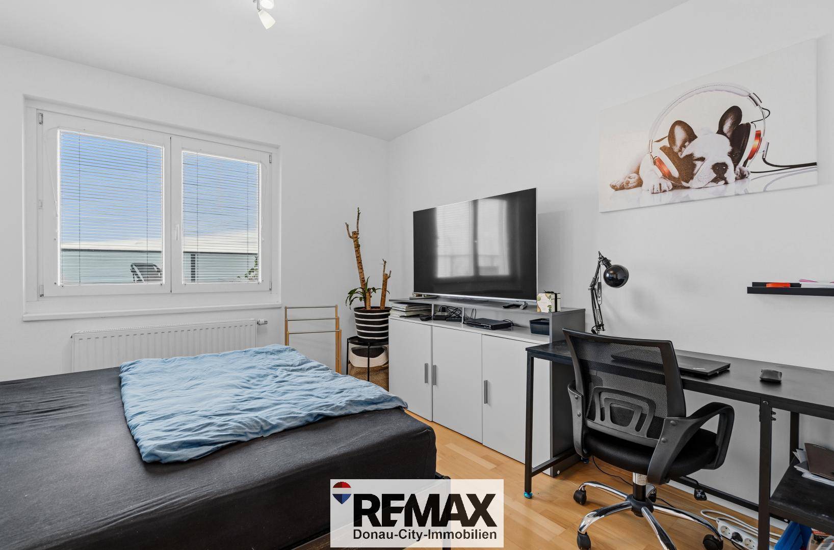 Schlafzimmer mit großem Fernseher, Schreibtisch und Holzboden.
