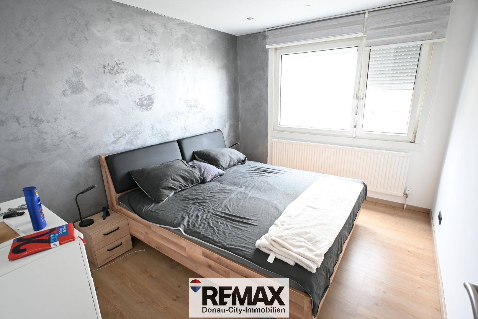 Schlafzimmer mit Doppelbett, Nachttischen und einem Fenster, die Wand ist modern gestaltet.