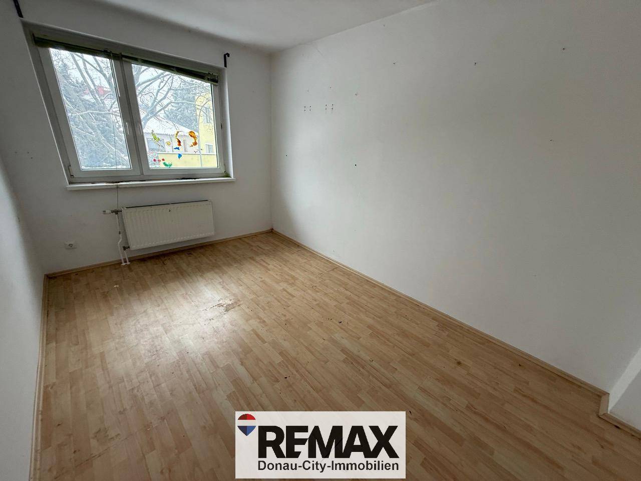 Helles Schlafzimmer mit Laminatboden und Fenster, das einen Blick nach draußen bietet.