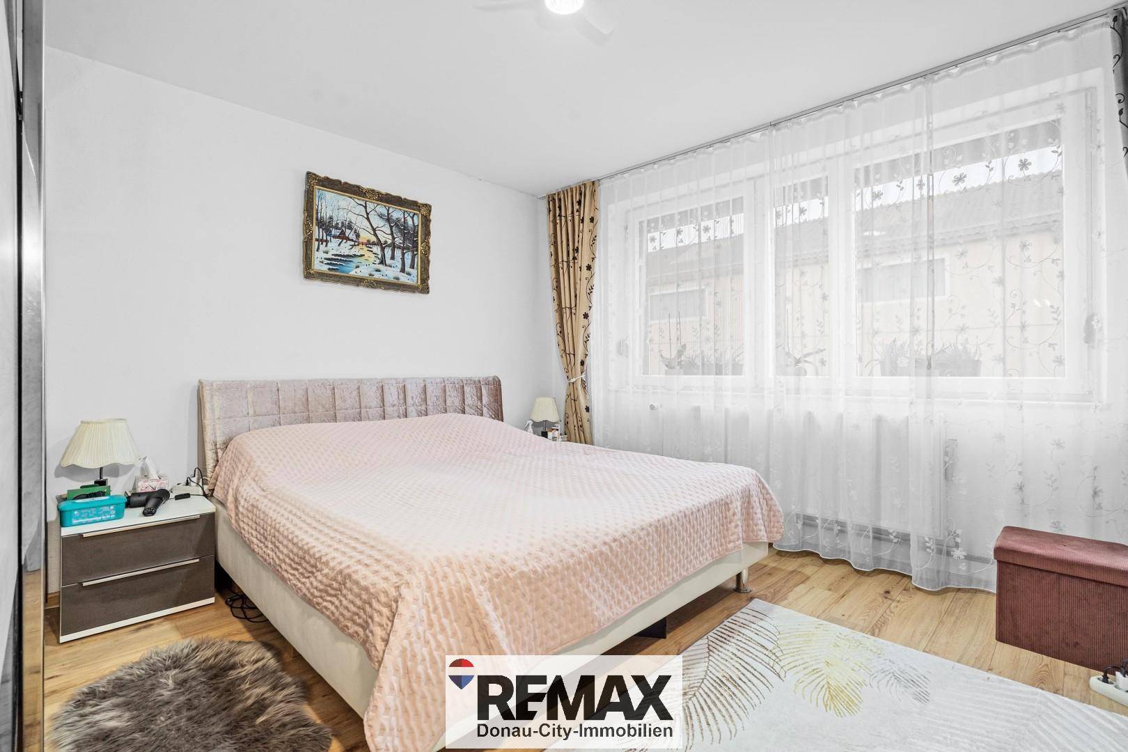 Helles Schlafzimmer mit großem Fenster, Doppelbett und modernem Nachttisch.