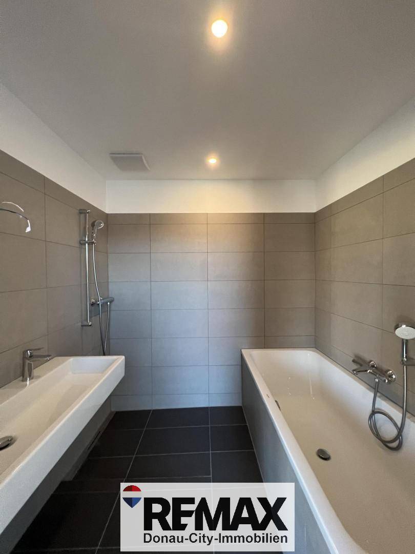 Helles Badezimmer mit Badewanne, Dusche und schwebendem Doppelwaschbecken.