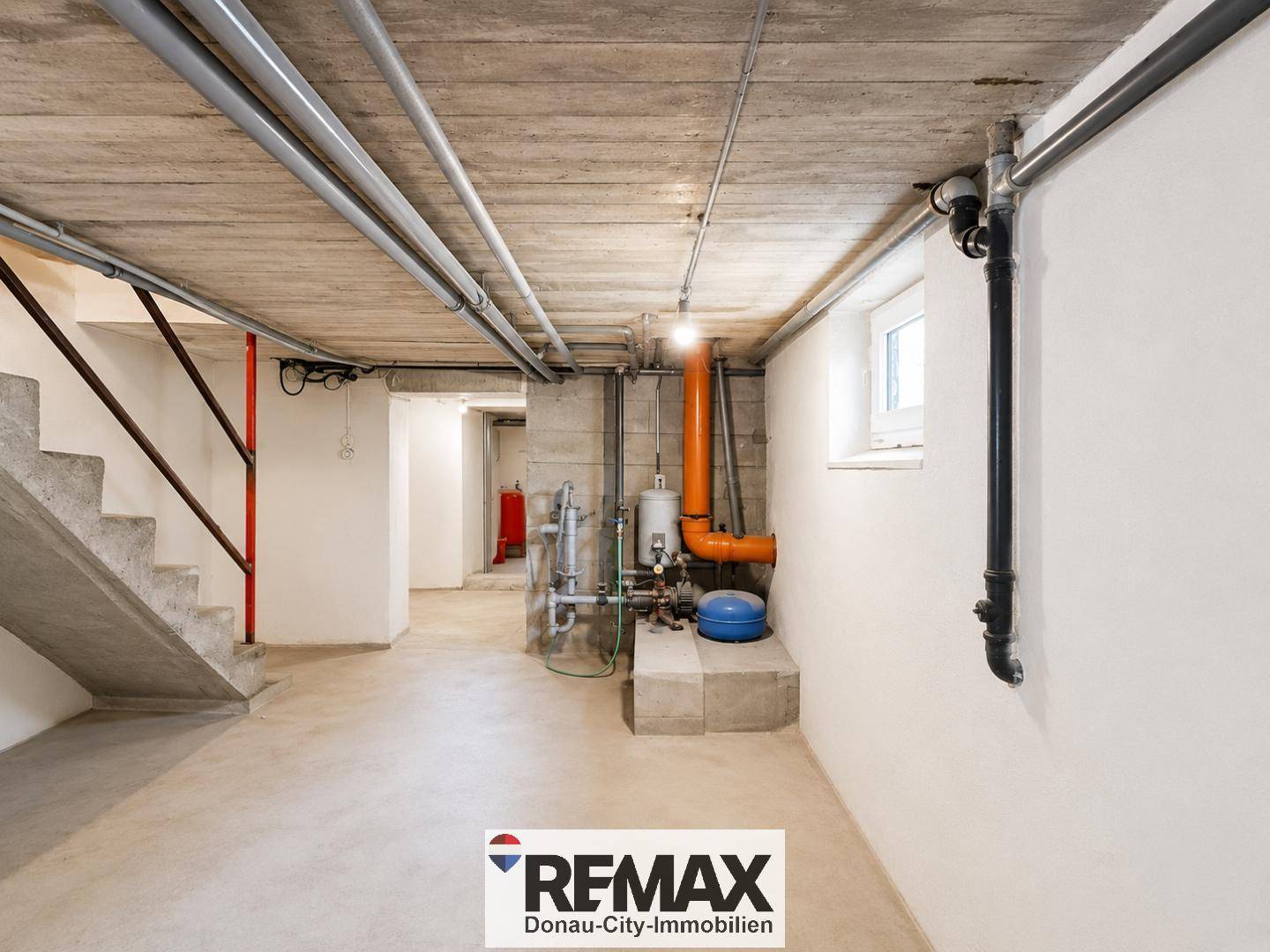 Kellerflur mit Betontreppe und sichtbaren Versorgungsleitungen an der Decke.