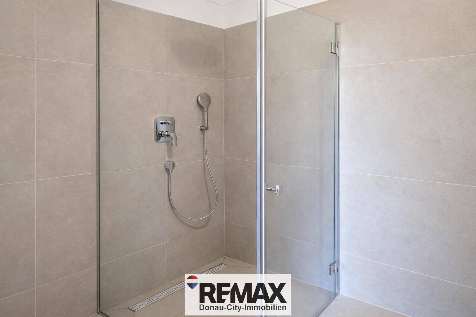 Geräumige Dusche mit Glasabtrennung und modernen grauen Fliesen.