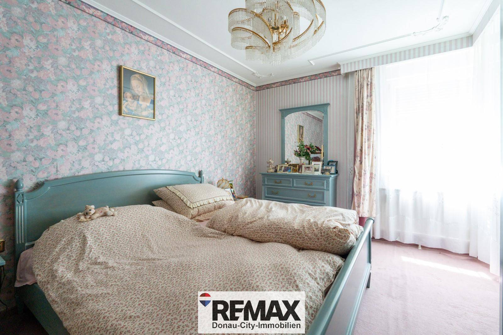 Schlafzimmer mit floraler Tapete, hellblauem Bettrahmen und passenden Möbeln.