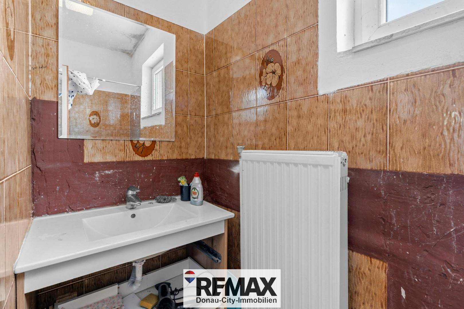 Badezimmer mit Waschbecken, Spiegel und Heizkörper, teilweise gefliest im Retro-Stil.