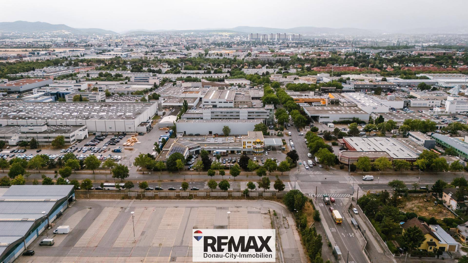 Luftaufnahme eines Gewerbegebiets mit großen Hallen, Parkplätzen und Straßen.