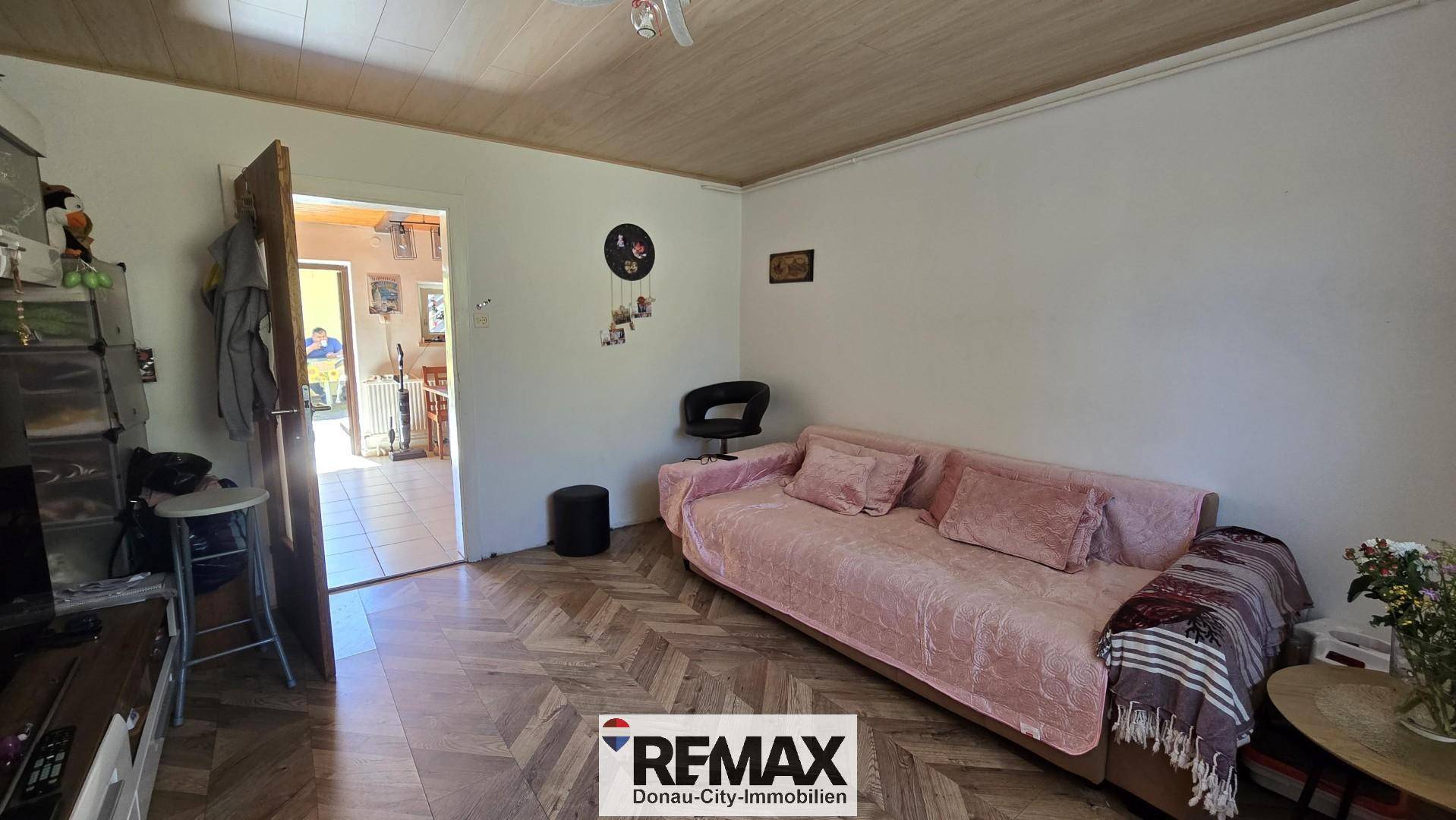 Wohnraum mit Sofa, Zugang zu einem weiteren Zimmer und Holzdecke.