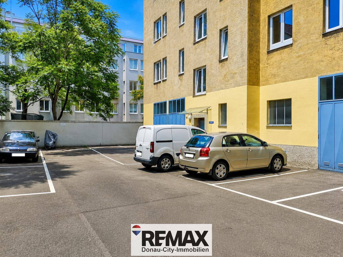 Außenparkplätze vor einem Wohngebäude mit Bäumen und weiteren Fahrzeugen in urbaner Umgebung.