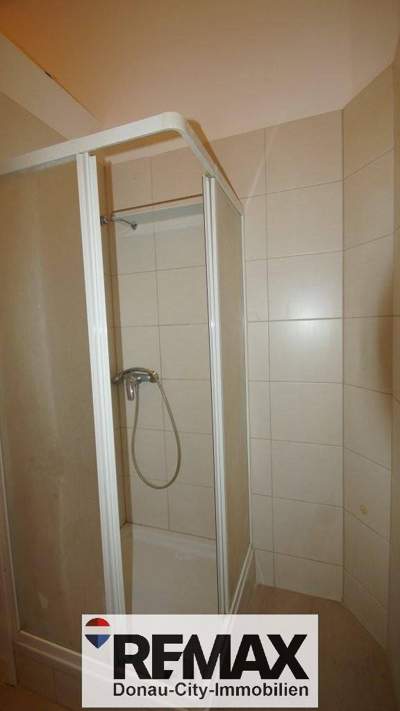 Duschkabine in einem gefliesten Badezimmer mit hellen Wandfliesen und Duscharmatur.
