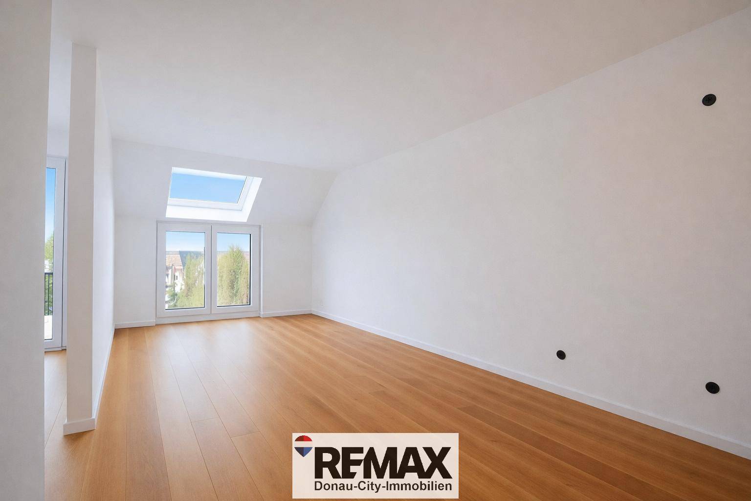 Helles, leeres Zimmer mit Holzboden, Dachfenster und Zugang zu einem Balkon.