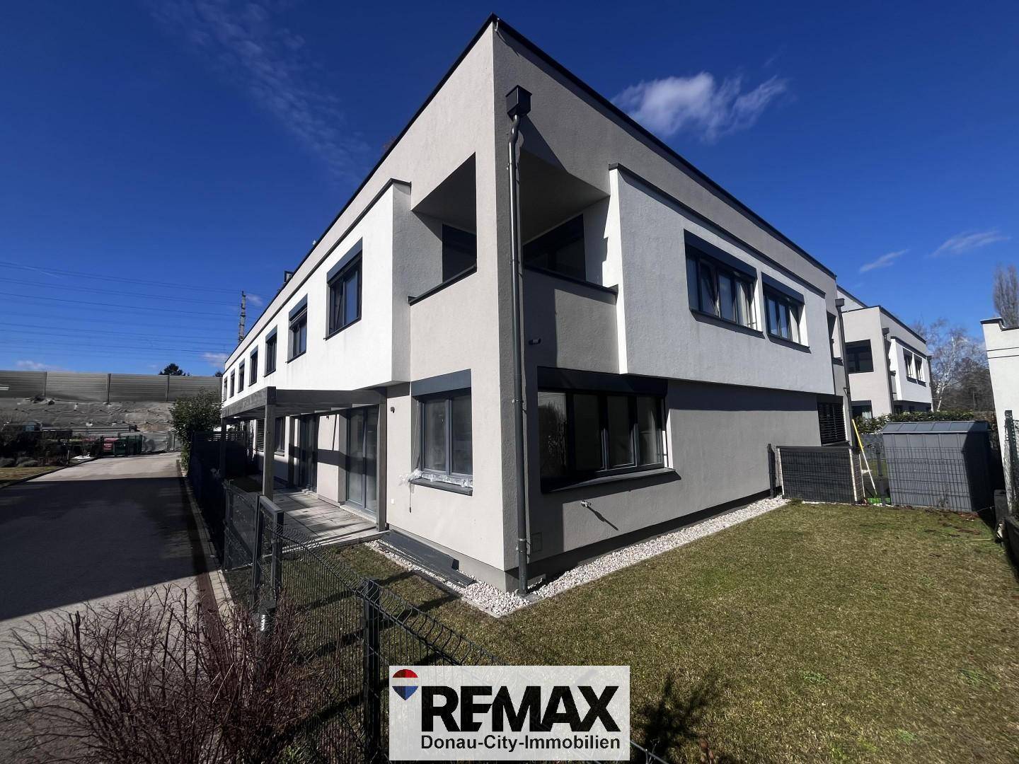 Moderne Wohnanlage mit privatem Gartenbereich und gepflegtem Rasen unter blauem Himmel.