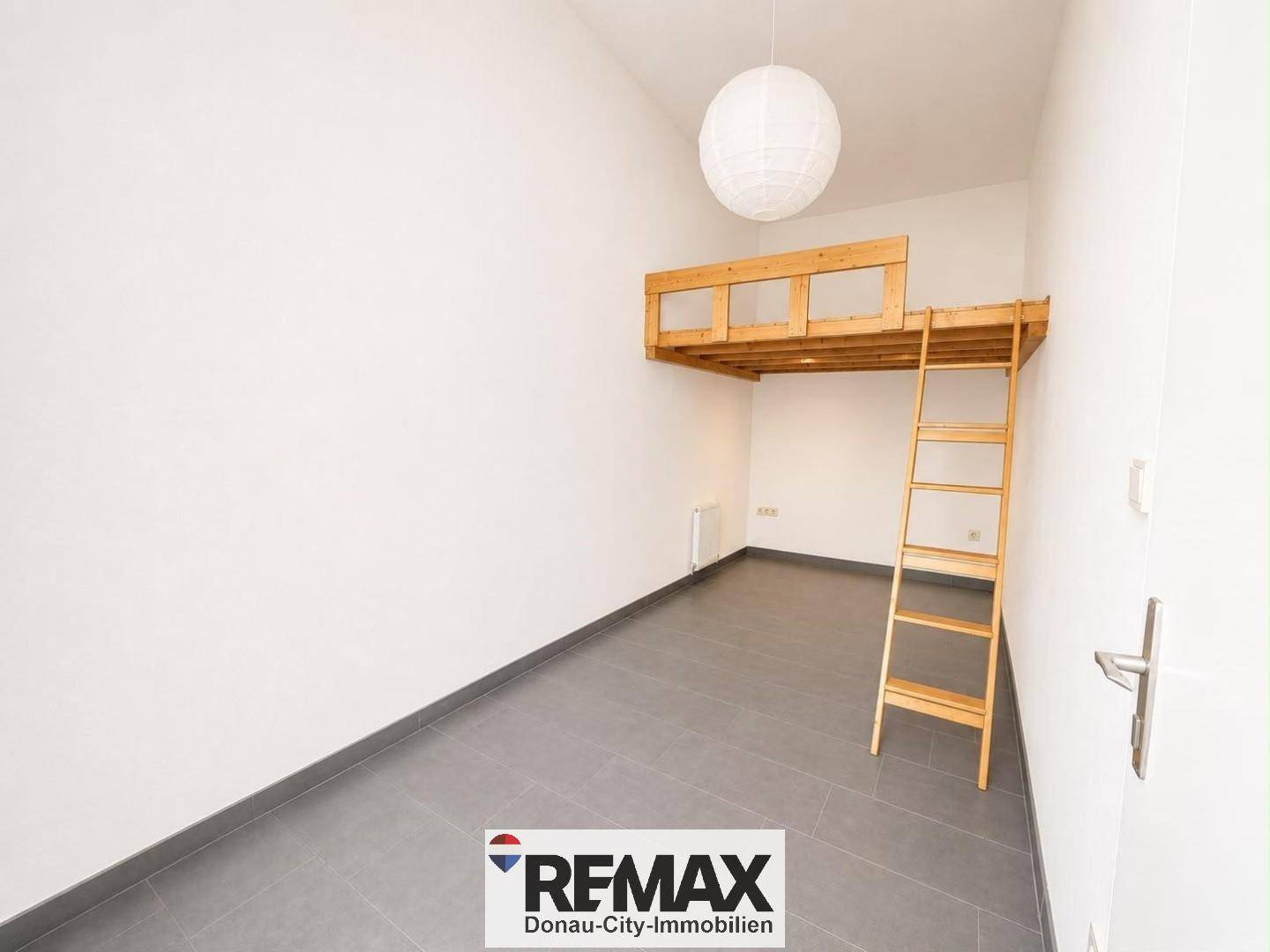 Geräumiges Zimmer mit Hochbett aus Holz und grauen Fliesen, bietet zusätzlichen Schlafplatz.