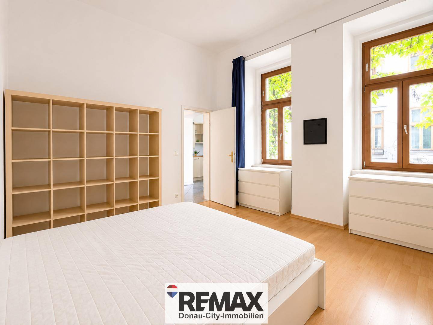 Geräumiges Schlafzimmer mit großem Regal, weißem Bett und zwei Fenstern für viel Tageslicht.