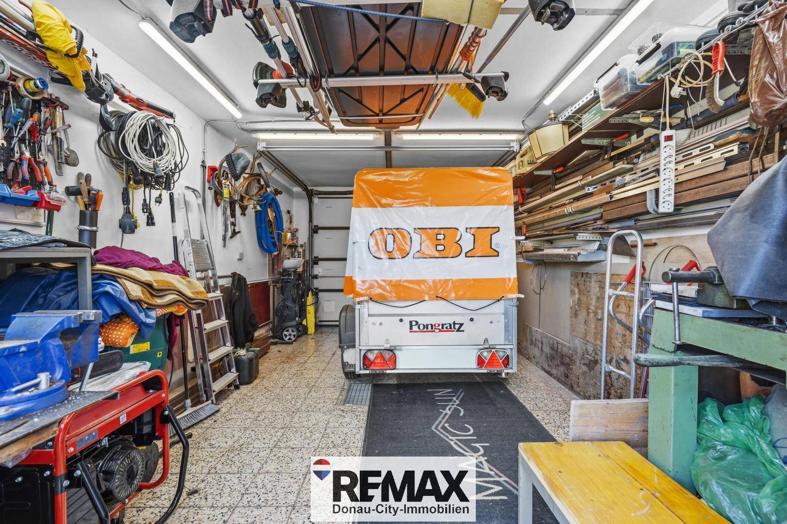 Geräumige Garage mit Rolltor, Anhänger und umfangreicher Werkzeugaufbewahrung an den Wänden.