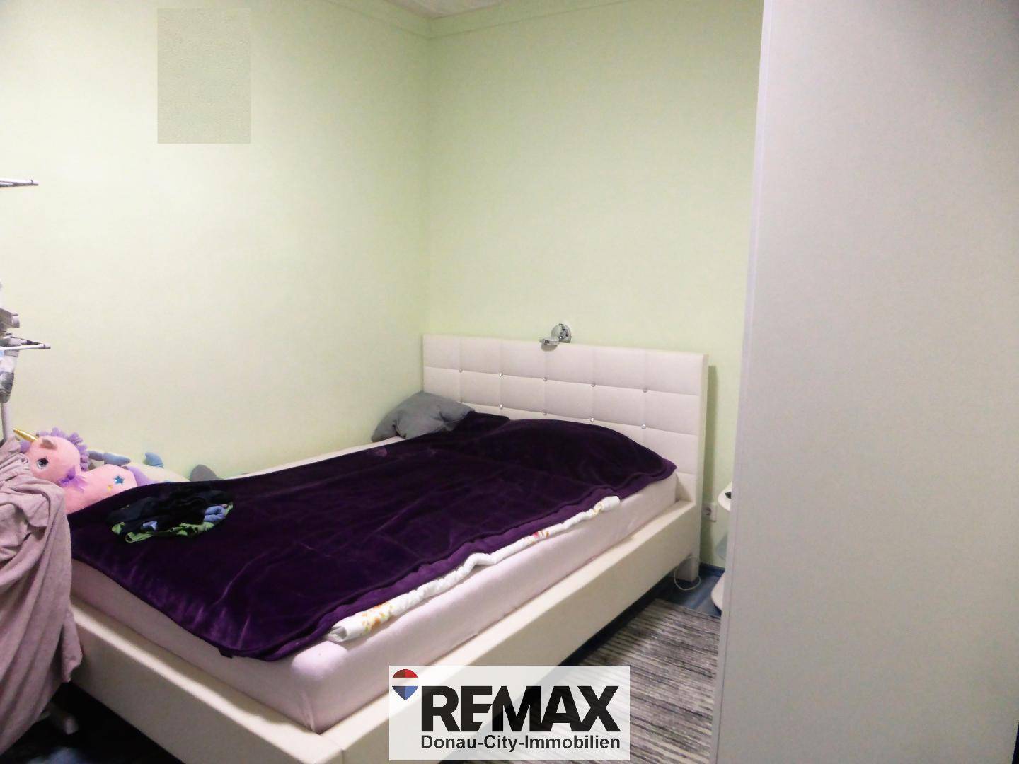 Schlafzimmer mit hellem Bett und grünen Wänden, ausgestattet mit Laminatboden.