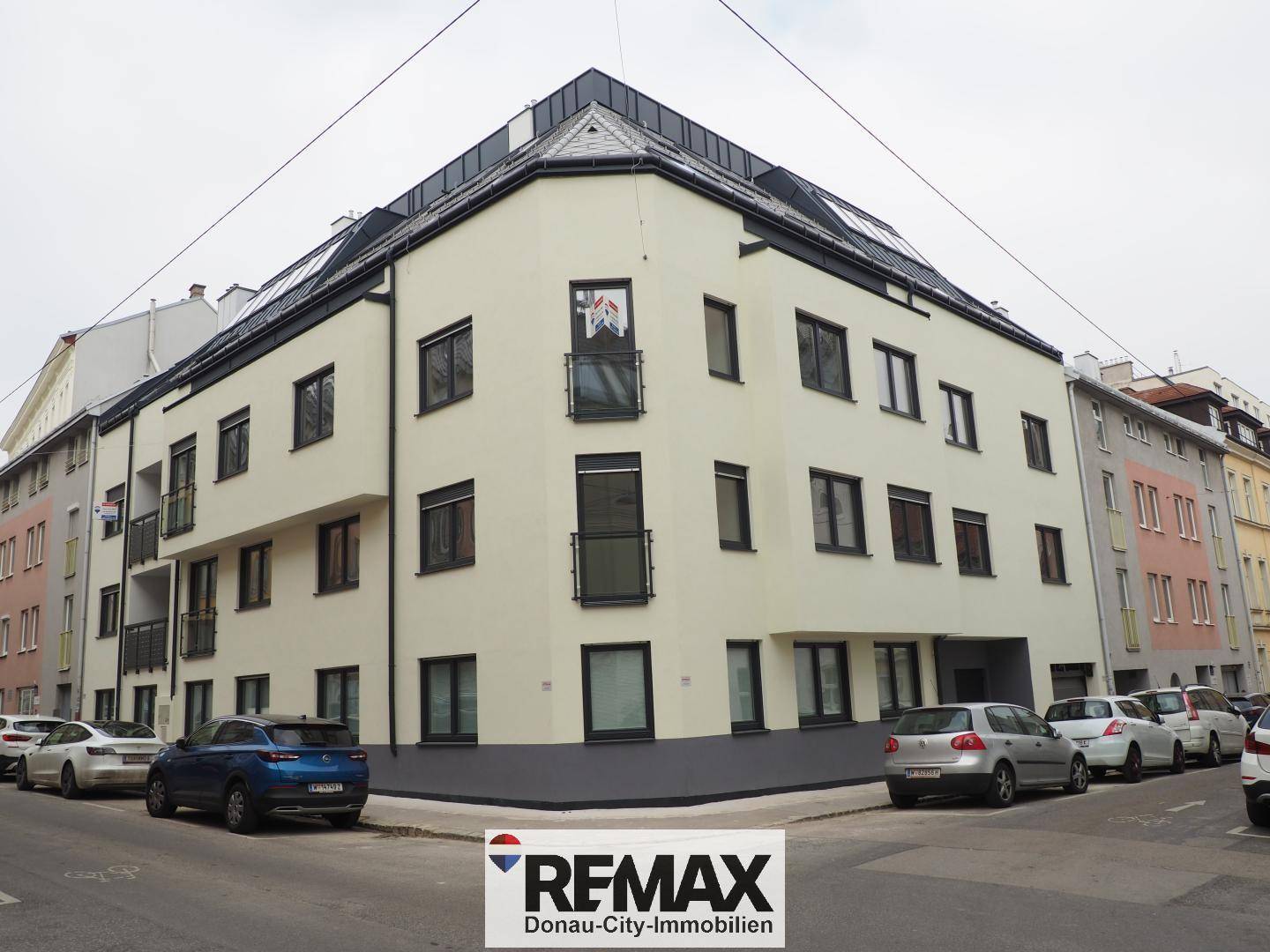 Modernes Eckgebäude mit heller Fassade und großen Fenstern an einer Stadtstraße.
