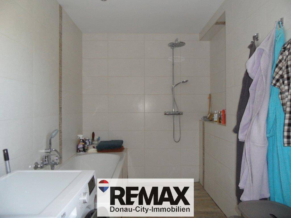 Modernes Badezimmer mit Badewanne, Regendusche und Waschmaschine, komplett gefliest.