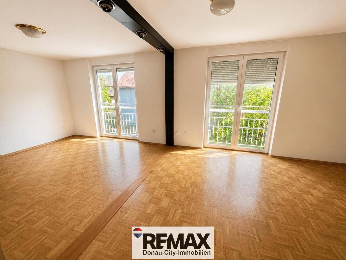 Großes, helles Zimmer mit Parkettboden und zwei französischen Balkonen, die den Raum erhellen.