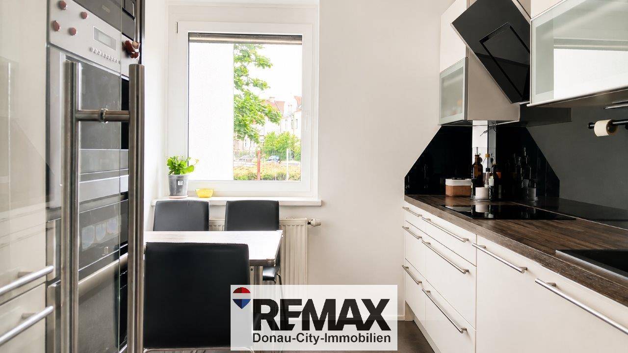 Moderne Küche mit weißen Schränken, dunkler Arbeitsplatte und Essbereich am Fenster.