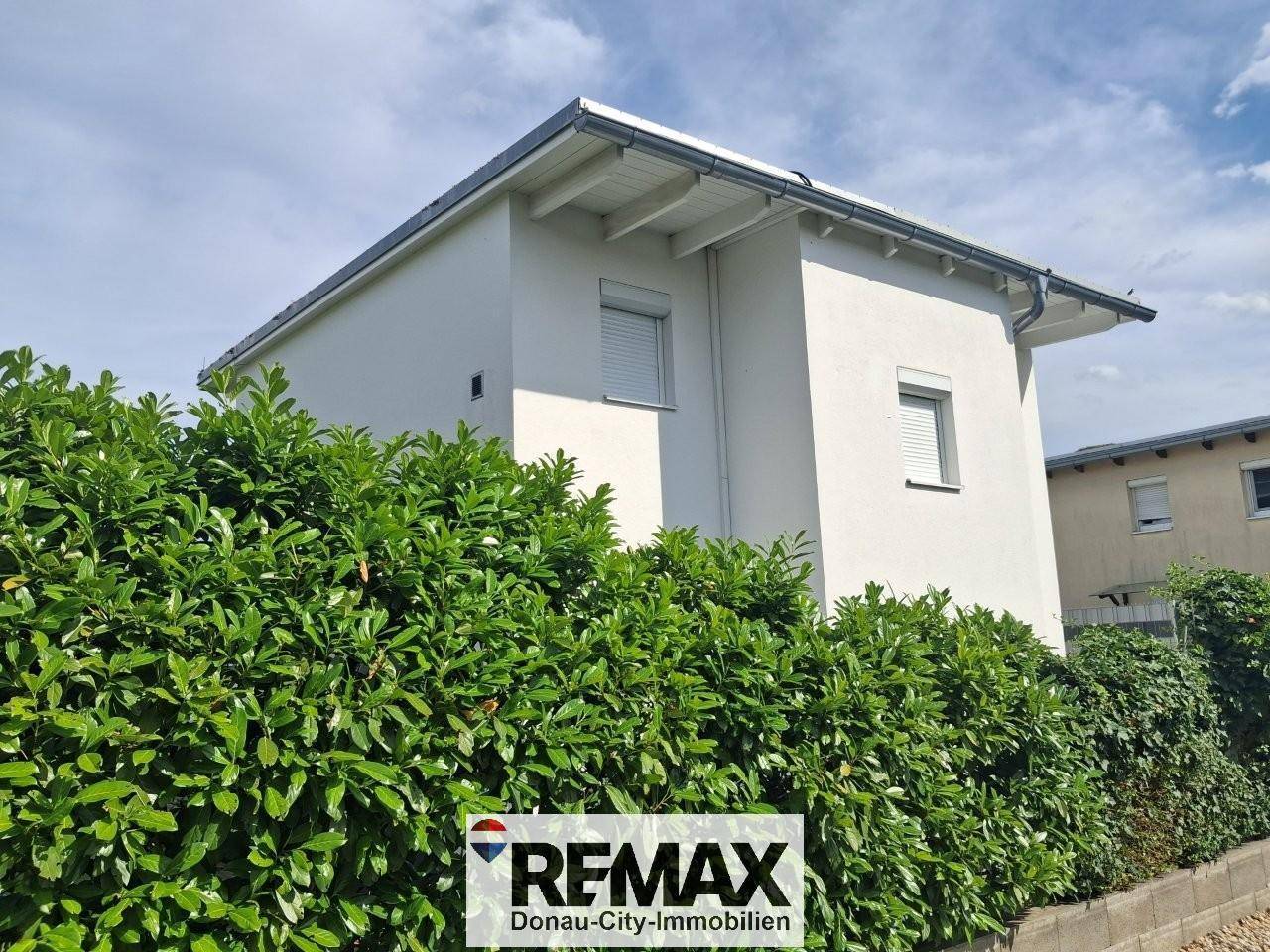Moderne Hausfassade in Weiß mit Rollläden und gepflegter Hecke im Vordergrund.