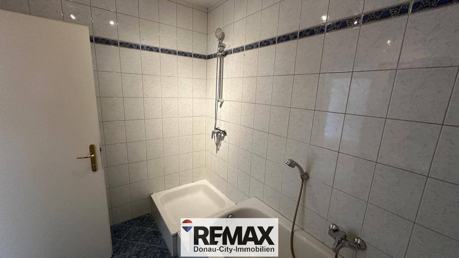Funktionales Badezimmer mit Badewanne und Duschvorrichtung, hell gefliest mit blauer Bordüre.