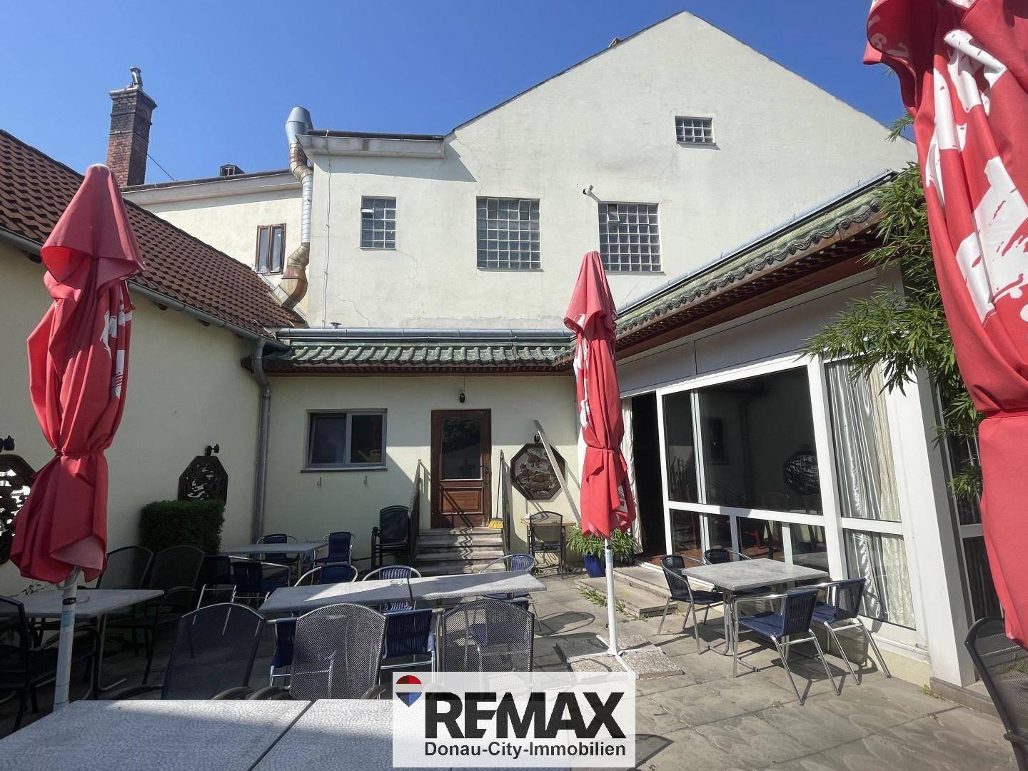 Hinterhof-Terrasse mit vielen Sitzgelegenheiten und roten Sonnenschirmen, ideal für gesellige Stunden.
