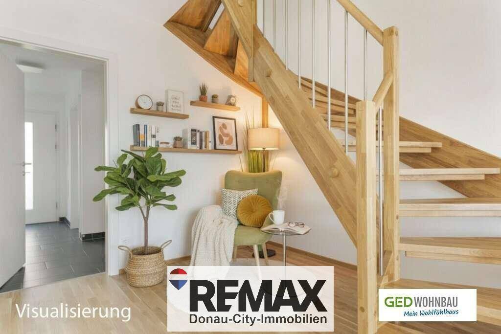 Heller Flurbereich mit offener Holztreppe, gemütlichem Sessel und dekorativen Wandregalen.