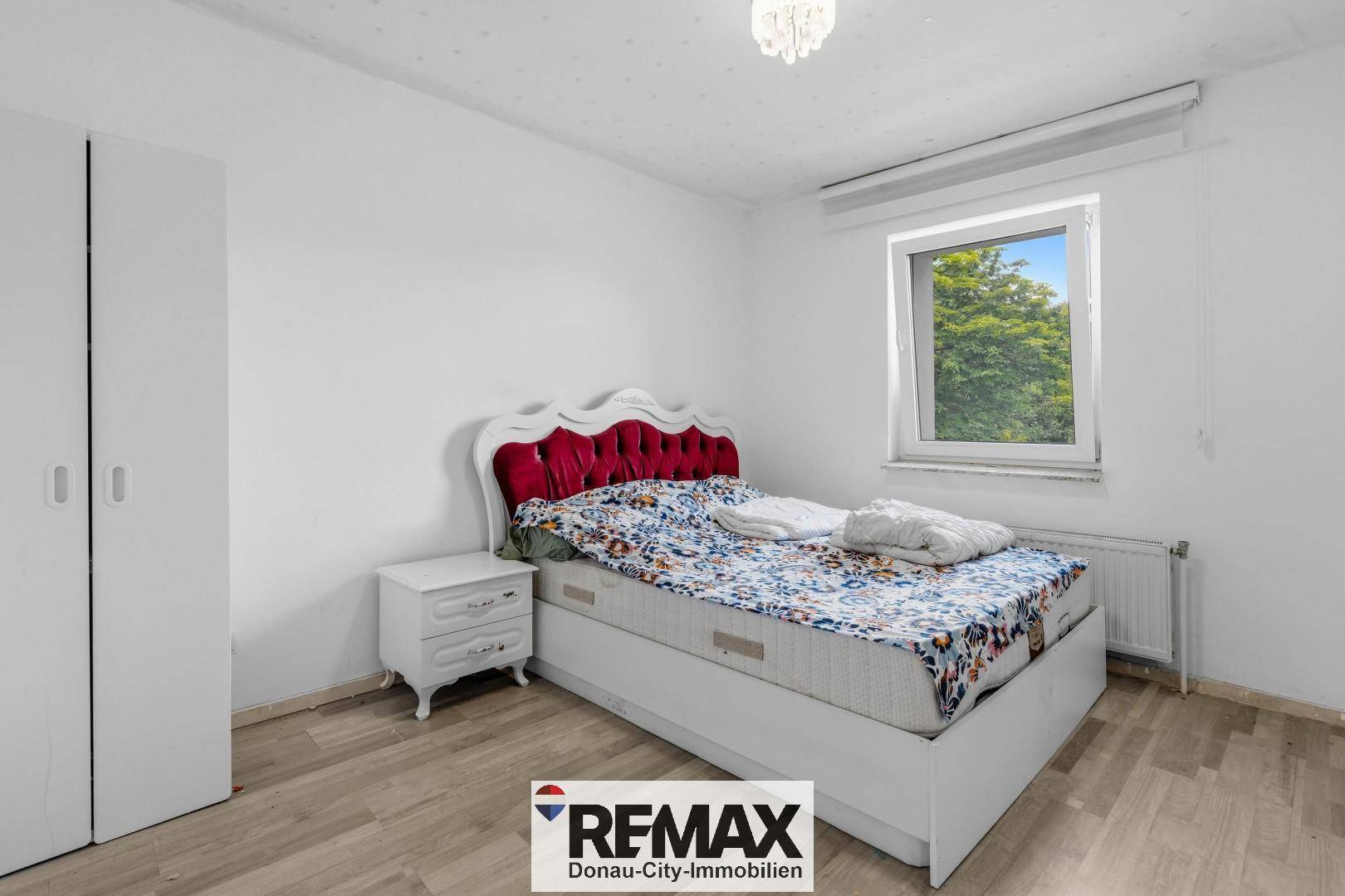 Schlafzimmer mit Laminatboden, weißem Bett und Fenster mit Blick ins Grüne.
